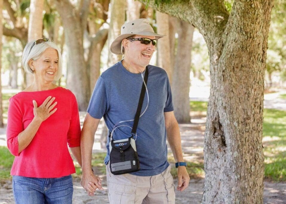 Couple walking outdoors with a portable oxygen concentrator